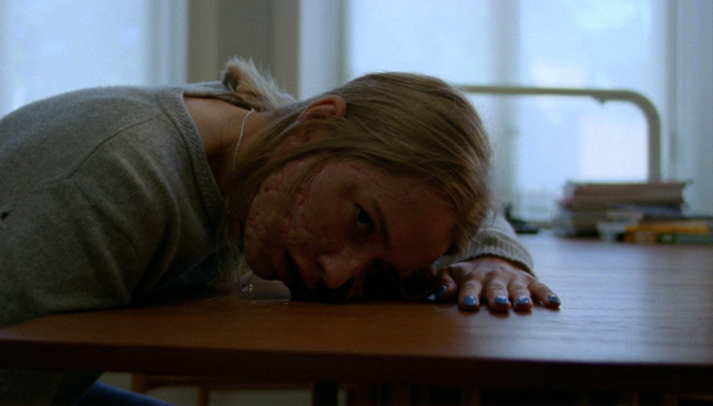 Kristine Kujath Thorp (Signe) con la faccia attaccata al tavolo in una scena di Sick of myself (2022) di Kristoffer Borgli 